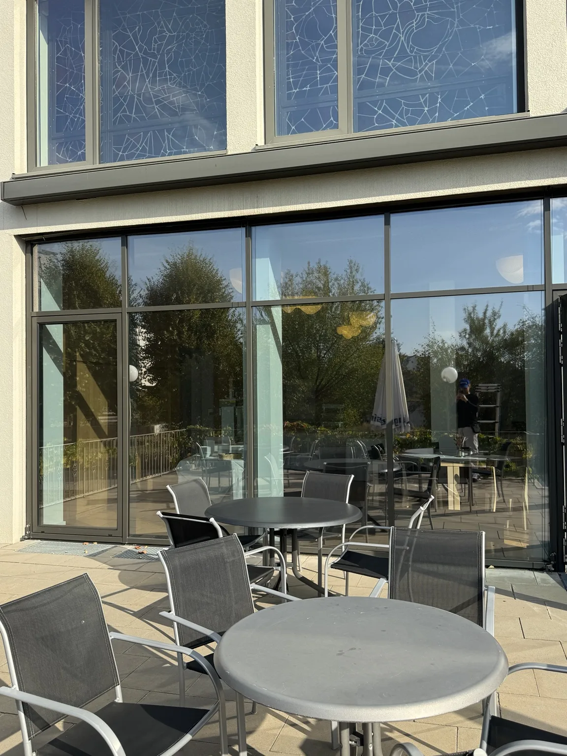 Verglaste Fassade des großen Speisesaals mit Terrasse, Tischen und Stühlen im Vordergrund